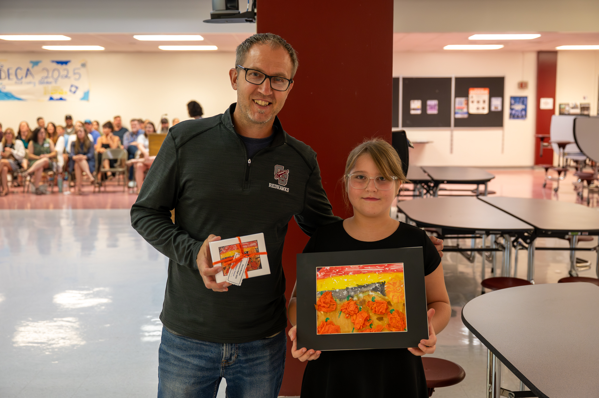 A board of education member standing proudly with a student, who gifted them artwork.